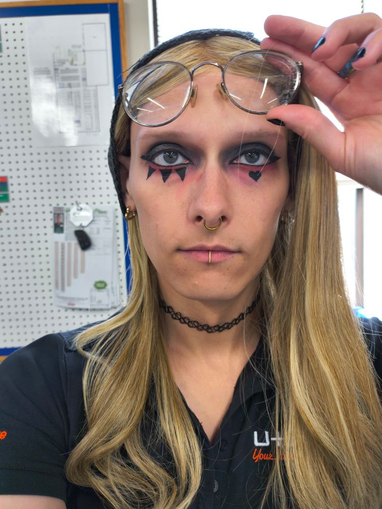 Amy at work
she has her glasses up to her forehead, gold jewelery (septum, ears, center lip), black choker, black work shirt
she has three eyeliner spikes under her right eye and a heart under her left. black eyeshadow on top red on bottom 