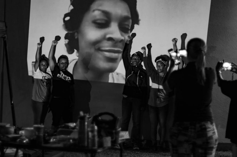 activists standing making fists in front of the jail where Sandra Bland died; her face is projected onto the wall of that jail