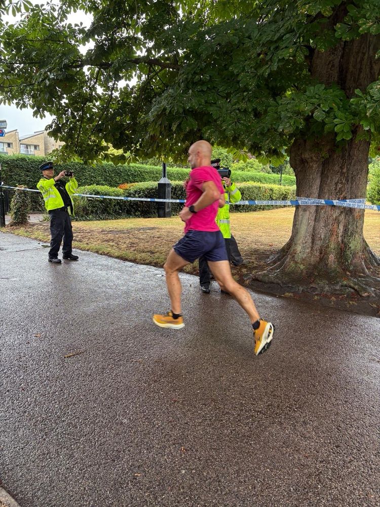 Policeman in hi viz with a speed gun pointed at parkrunners running down finish straight 
