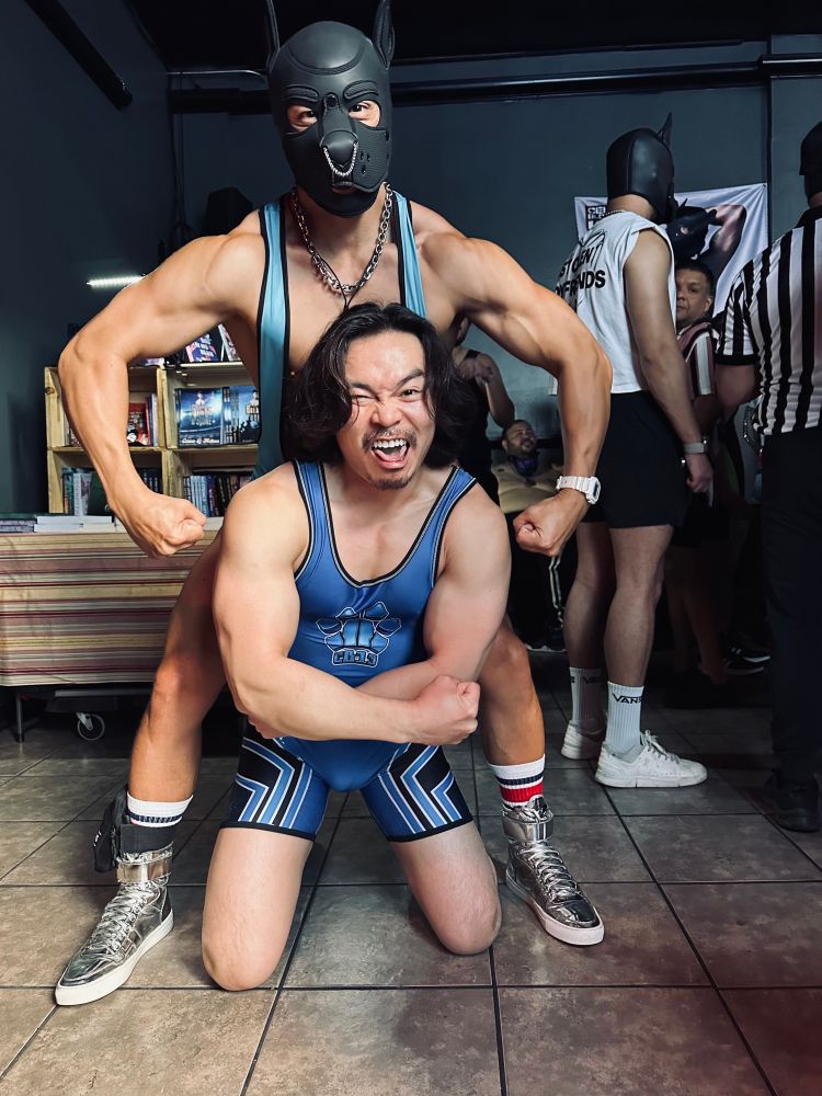 Two gays in singlets. One has a pup hood one, the other made a weird face. 