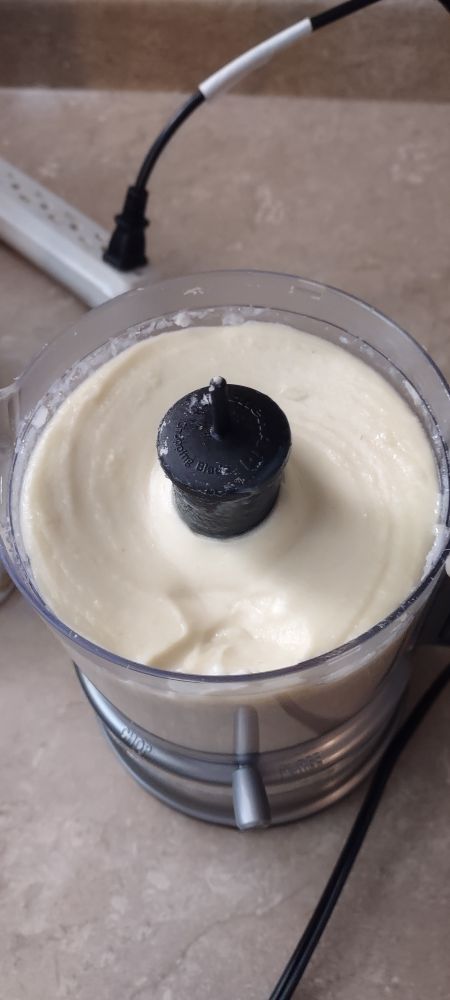A food processor with white taro paste inside. The processor is sitting on a brown marble countertop, behind it is a white power strip it's plugged into