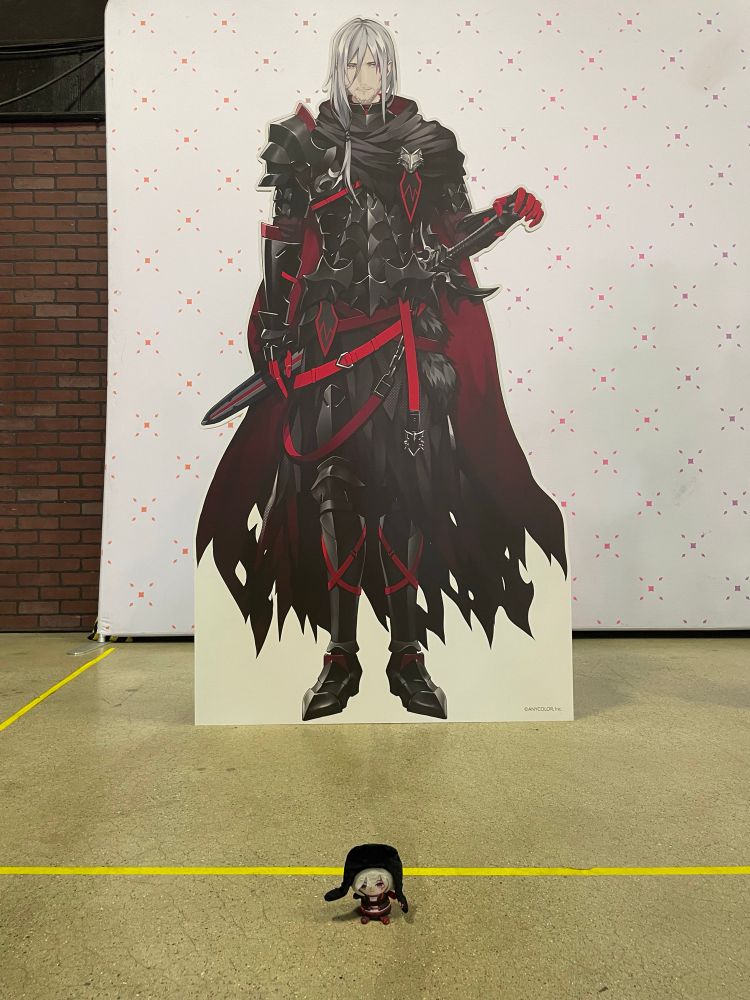 Fulgur puppet sitting on the floor in front of the Fulgur standee