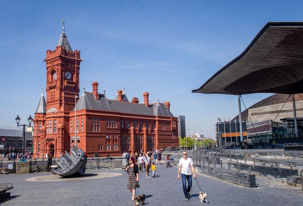 People walking outside Pierhead and Senedd Cymru (Welsh Parliament) buildings at Cardiff Bay.