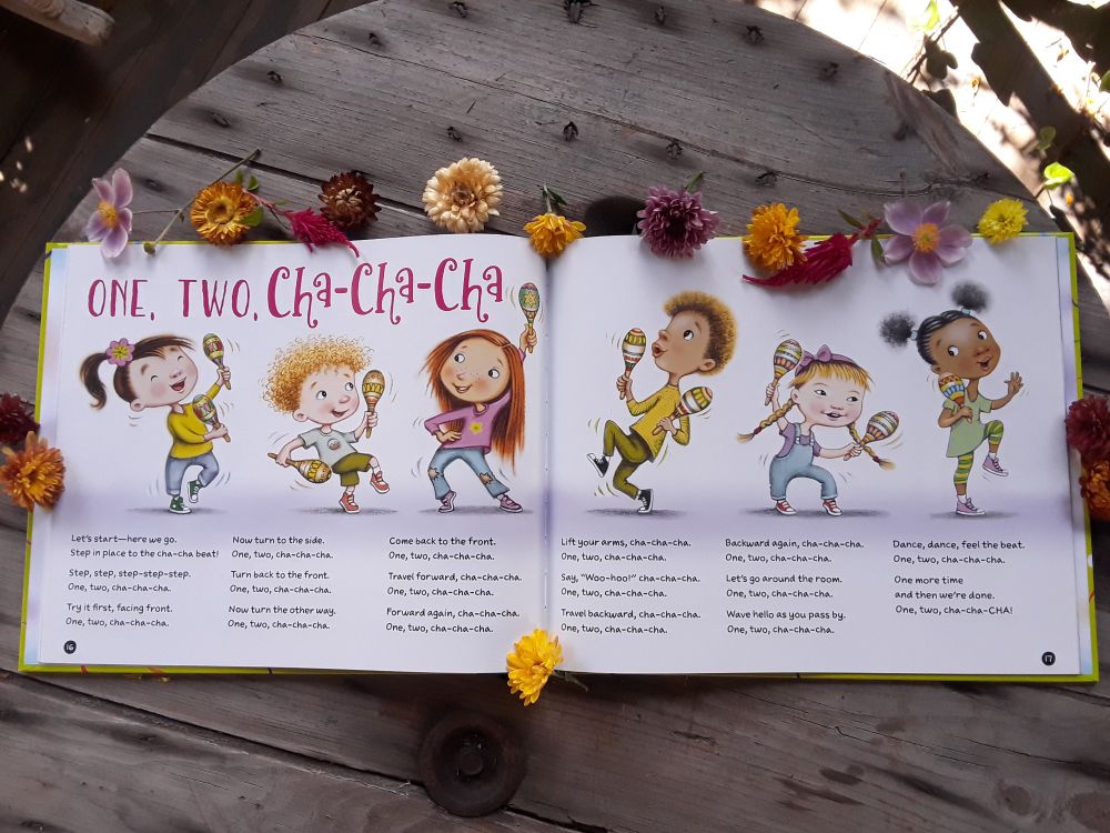 An open book illustrated with  dancing kids, and  autumn flowers are placed  around it.