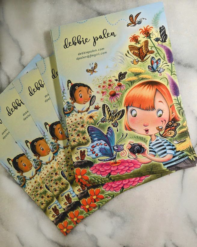  A photo showing a small stack of postcards , featuring the image of a butterfly garden and two girls  looking at and taking pictures of butterflies .