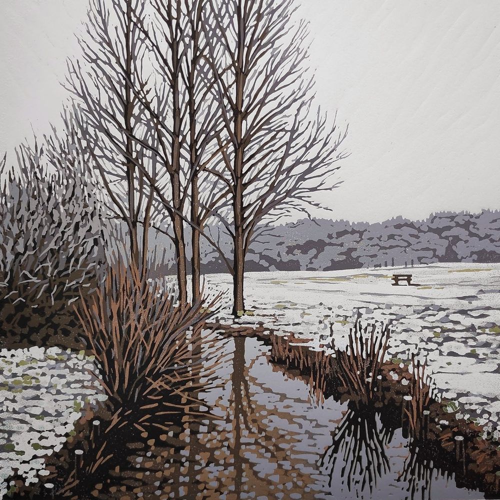 Print featuring a narrow river with a field and trees on both sides, the fields are covered in a light dusting of snow, the river shows reflections of the trees abd the sky is grey
