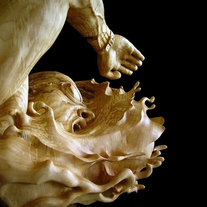 Carved wooden sculpture of the front of a person swimming in mid stroke with arm raised in rippled water