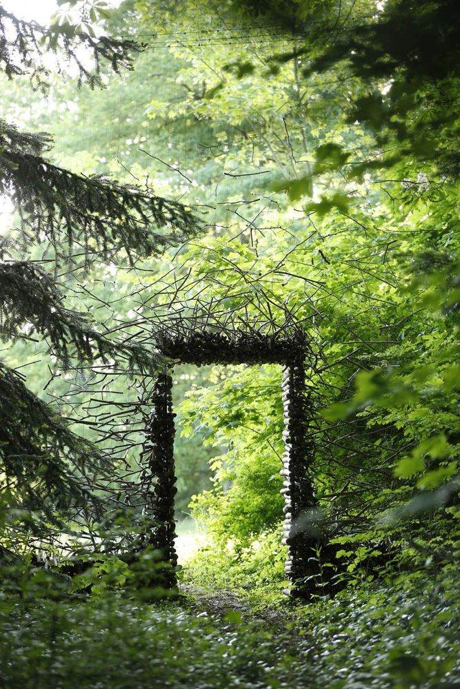 Photo of an outdoor art installation featuring a woodland with a magical looking doorway created by wood and twigs in the forest