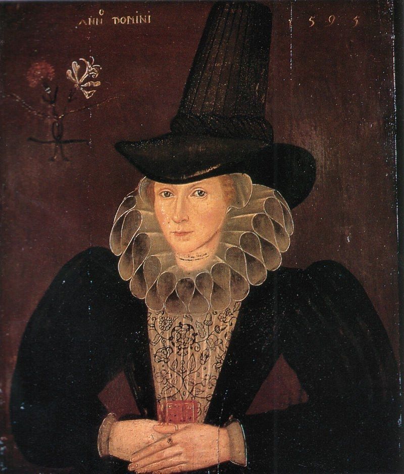 Painting featuring the upper half of a white woman with tall black pointed half, ruff and black dress, looking outwards with hands together 
