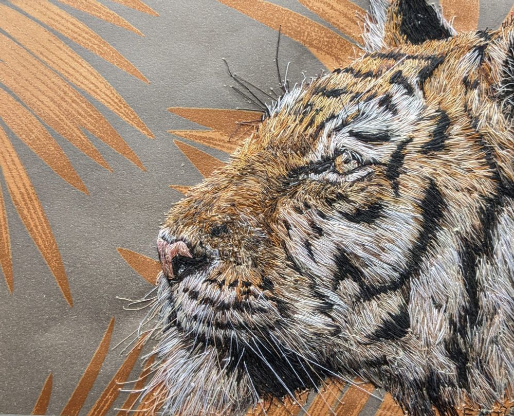 Embroidery of the head of a tiger facing left with brown leaves in the background 