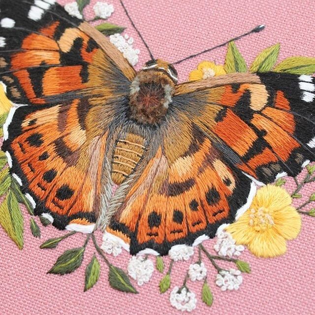 Embroidery of an orange butterfly with black markings on yellow flowers and pink background 