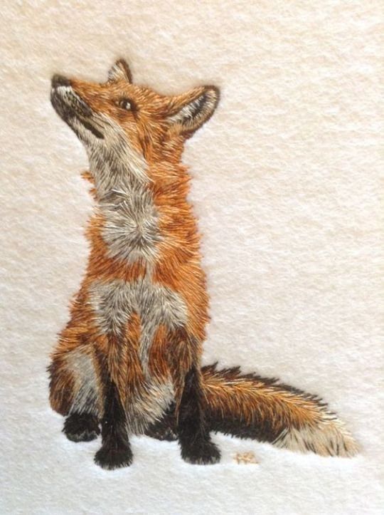 Embroidery featuring a sitting fox facing forwards and looking up to the left with bushy tail on the ground to the right, all on a cream background 