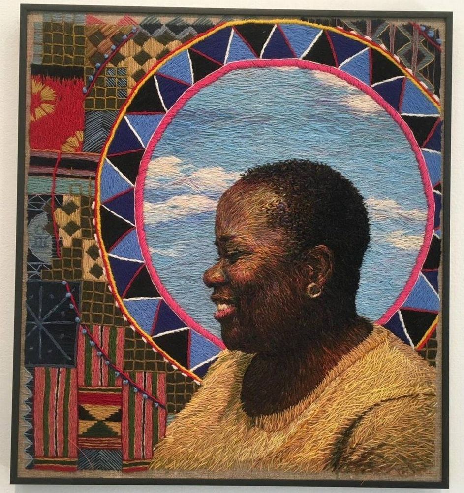 Pictorial embroidered artwork featuring the head and shoulders of a Black woman facing left with short hair yellow top and smiling, the subject is presented within a decorative circle and with embroidered patterns to the left