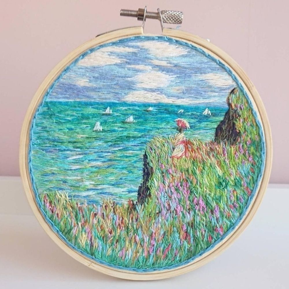 Embroidery hoop with embroidered scene of a view towards the sea from grassy clifftops