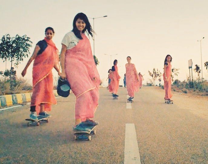 Photo of a road filled with Indian women in pinkish saris on skateboards moving forwards