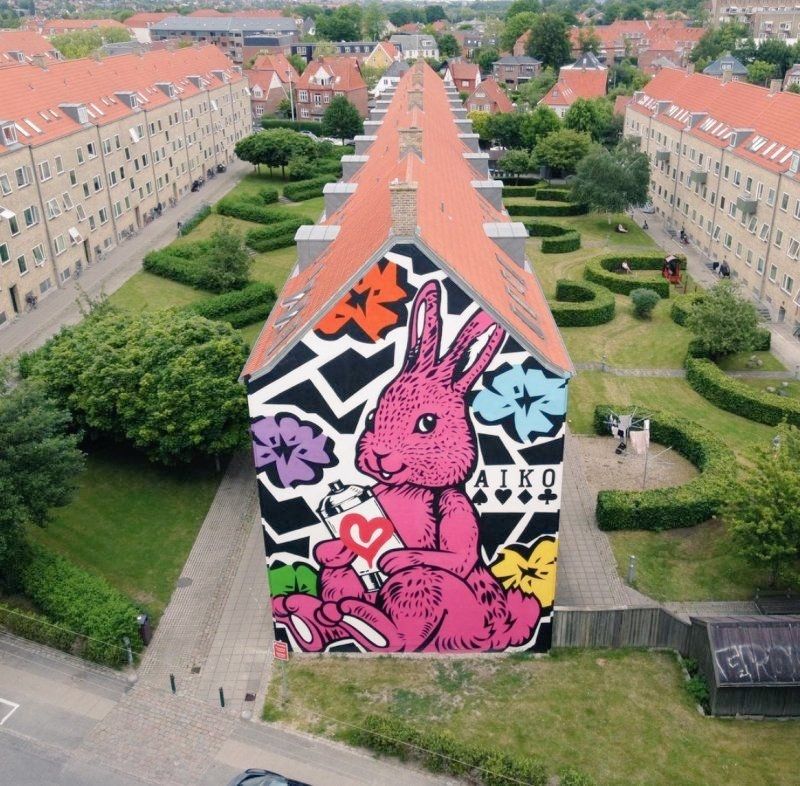 Photo looking from slightly above at three rows of houses with gardens between, the end of the middle row has a large mural of a sitting comic style pink rabbit and flowers 
