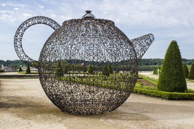 Large sculpture in an outdoor setting of a round teapot created with lace-like metal patterns