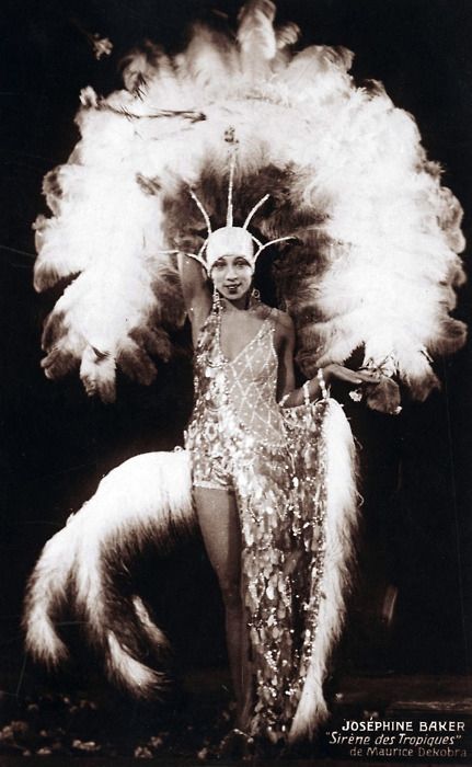 Monochrome photograph featuring a standing Black woman facing forwards dressed in stage costume with glittery dress and featheted headdress