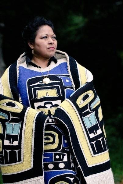 Photo featuring a standing woman wearing a cloak with significant symbols and motifs in black yellow and blue