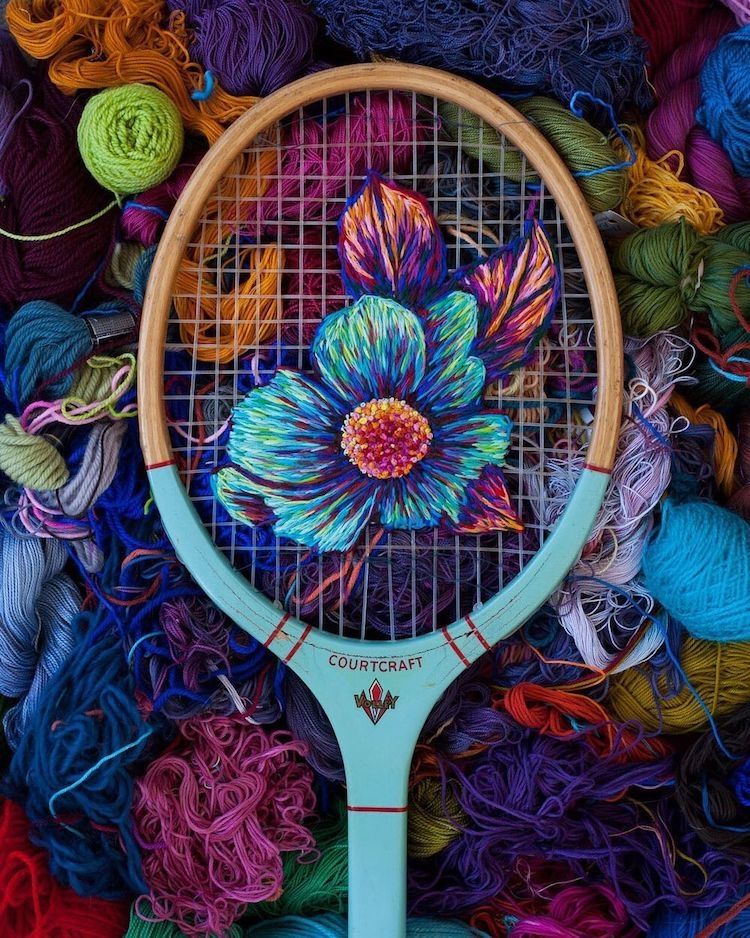Photo of a sports racket with flower design created with brightly coloured yarn in the strings against a backdrop of coloured threads