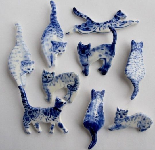 Photo featuring nine ceramic cat brooches in blue and while grouped together on a white background 