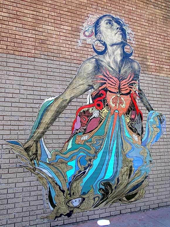 Street artwork with a colourful print of a woman in flowing dress as if rising from a brick wall 