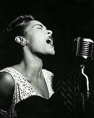 Monochrome photograph featuring a Black woman, head and shoulders facing right, while singing into a metal microphone with head up, eyes closed and mouth open, all against a dark background 
