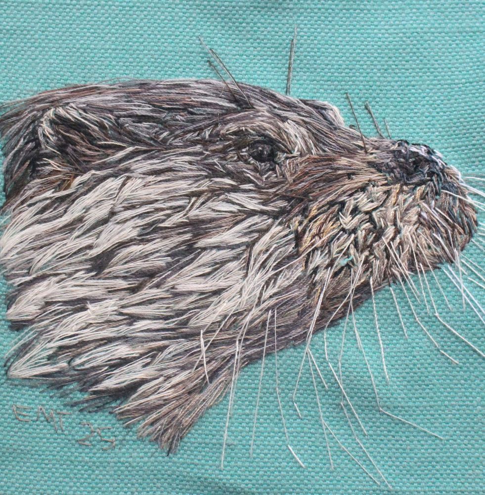 Pictorial embroidery textile artwork featuring the head of an otter facing right with wet looking fur against a turquoise background 
