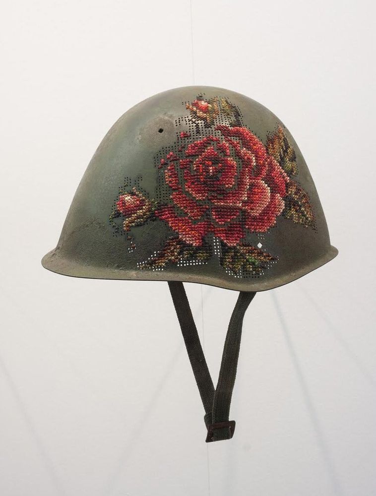 Photo featuring a soldier's green helmet with embroidery of a red rose on the side