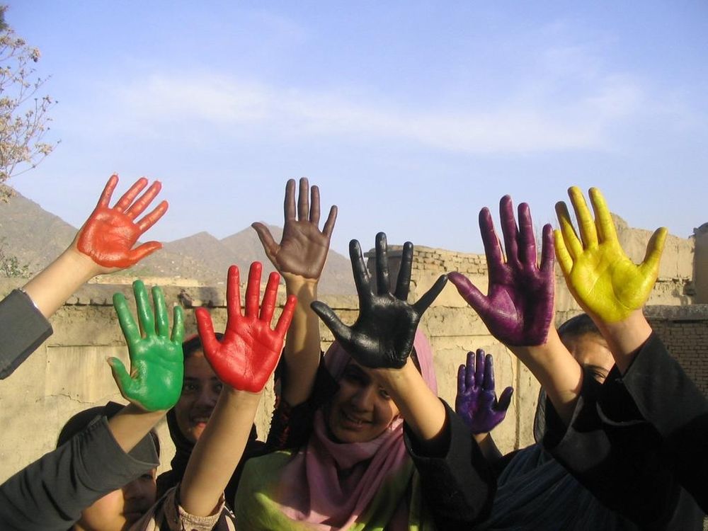 Photo of hands covered in different coloured paint raised in an outside setting