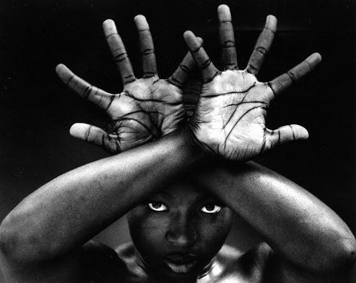Monochrome photograph of a Black young wonan holding her hands over her head with palms outwards and fingers wide