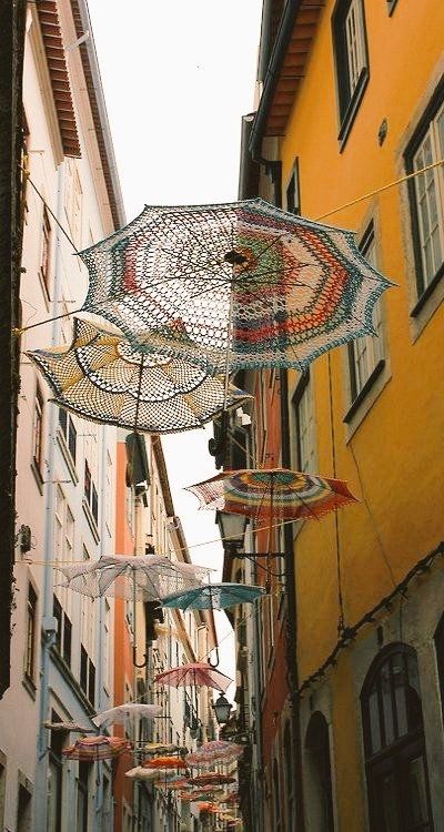 Photo of umbrellas with crochet shades hanging between buildings over a street in a Portuguese town