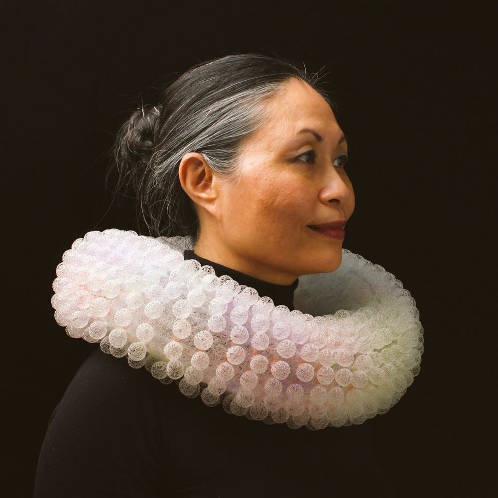 Photo featuring the head and shoulders of a woman facing right wearind a white ruff like creation around her neck 