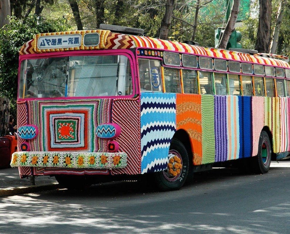 Bus covered in multicoloured crochet on a sunny street 