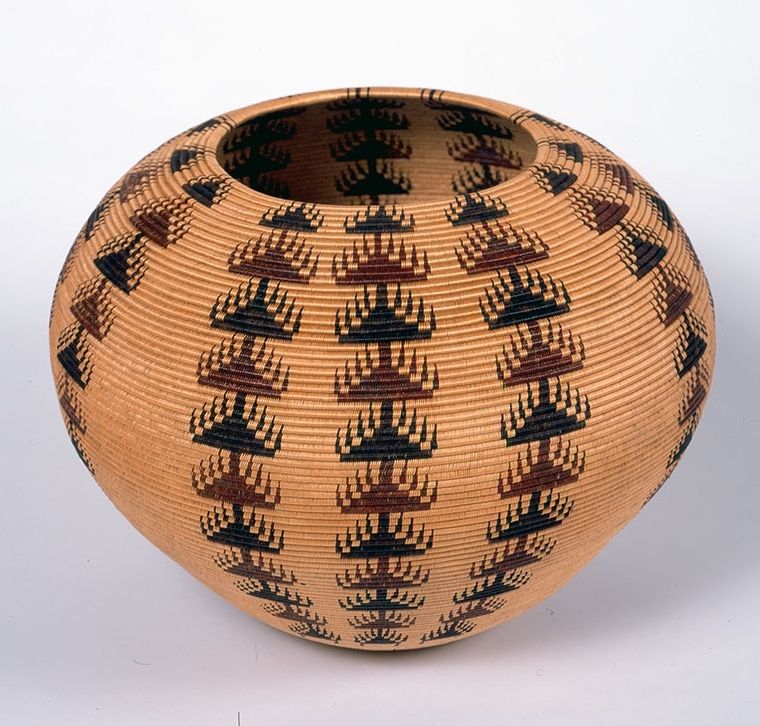 Photo of a round woven basket with narrow base and wider top decorated with repeated triangular brown and black symbols in vertical lines