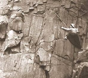 Sepia photograph featuring two women rock climbers wearing long dresses and hats climbing a craggy rock face