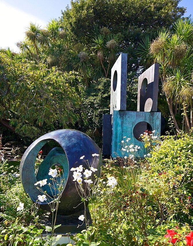 Garden with large bronze geometric scultures amongst trees and flowering plants