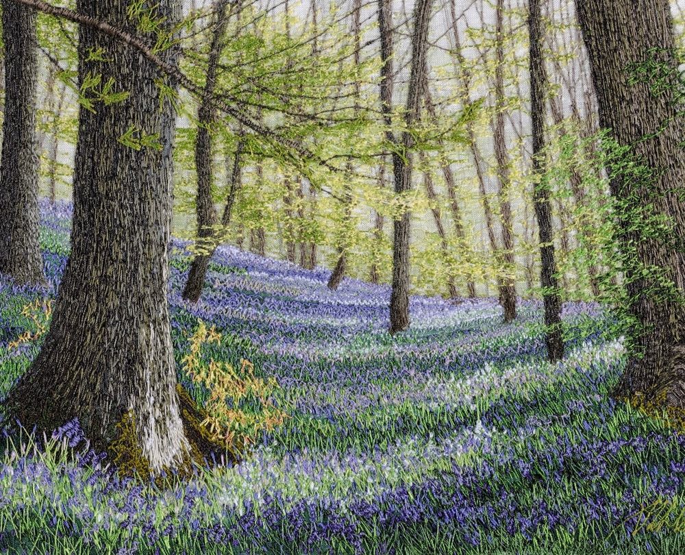 Pictorial textile artwork featuring a woodland in the dappled sunshine with woodland floor covered in purple flowers and green foliage 