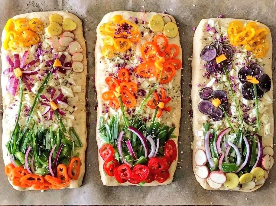 Photo featuring three rectangular loafs of bread decorated with slices of vegatables such as red onion and peppers to create images of plants with flowers