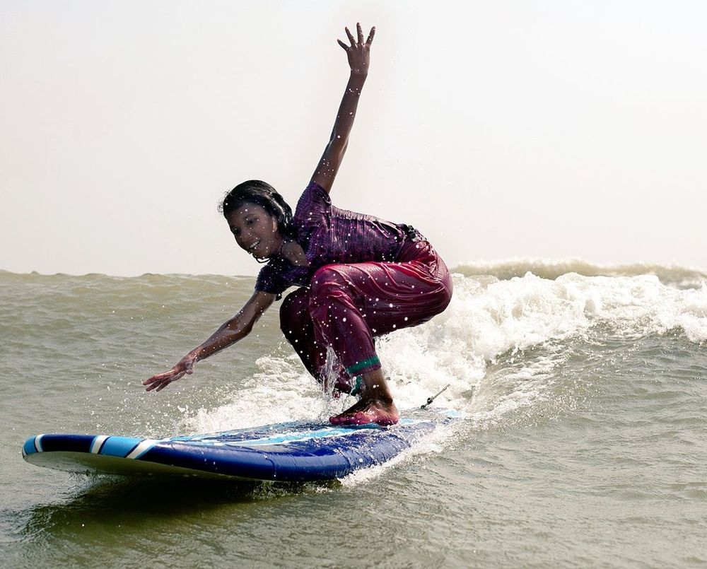 Young woman surfing a small wave, crouching with arms out