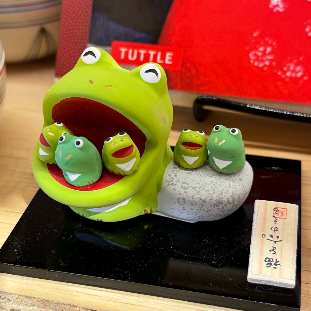 A little figuring of five frogs. One giant frog has three small frogs in its mouth. Two small frogs sit on a rock next to it