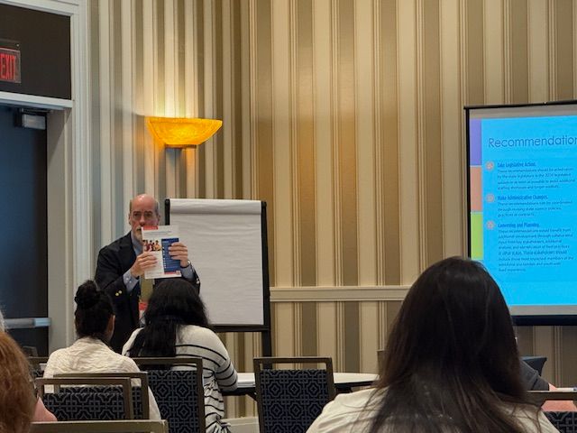 CT DCF's Frank Gregory holds up a copy of Connecticut's strategic plan to strengthen the behavioral health workforce for Institute attendees.