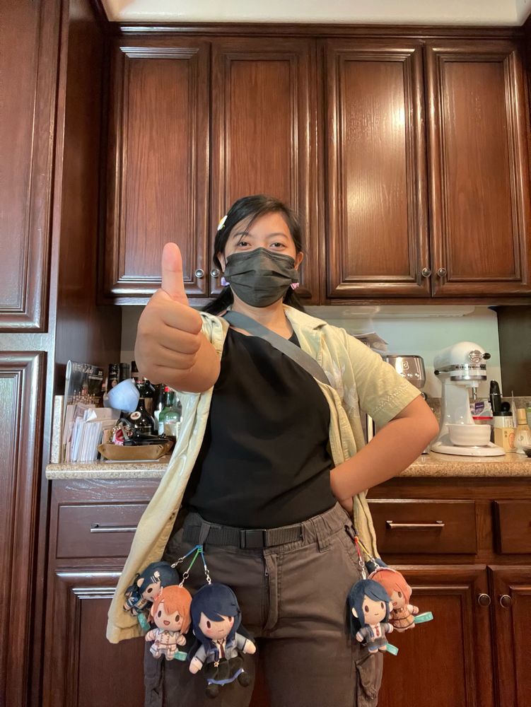 A picture of IRL eggu, facing the camera and giving a thumbs up. Several tiny plushes of Ichika Hoshino and Minori Hanasato from Project Sekai: COLORFUL STAGE! feat. Hatsune Miku are strapped to their pants's belt loop and D-ring.