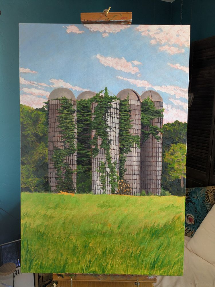 An oil painting nearing completion of some silos covered in vines behind a grassy field. The sky is blue with a light scattering of clouds, and there are dense trees behind the silos.