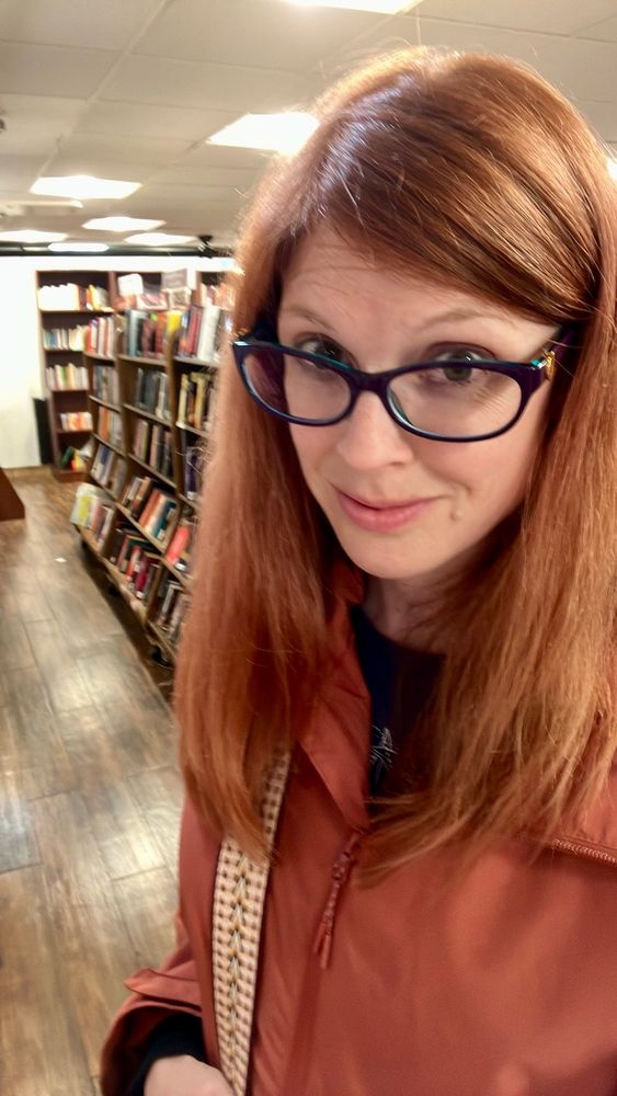 Woman with red hair and orange jacket in a bookstore