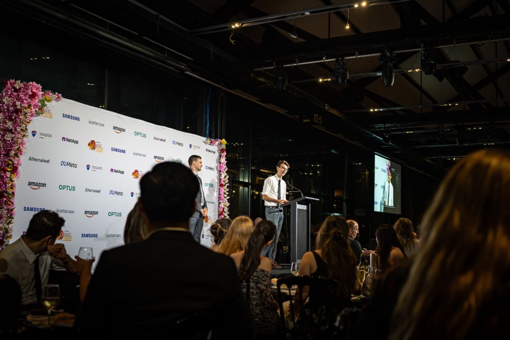 Julian Fell speaking at a lectern, with formally dressed people watching from their tables