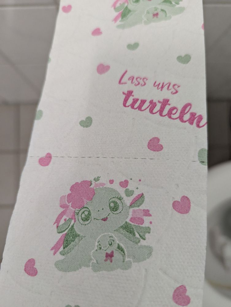 Toilettenpapier auf das zwei Schildkröten und der Spruch "Lass uns turteln" in pink und grün aufgedruckt sind