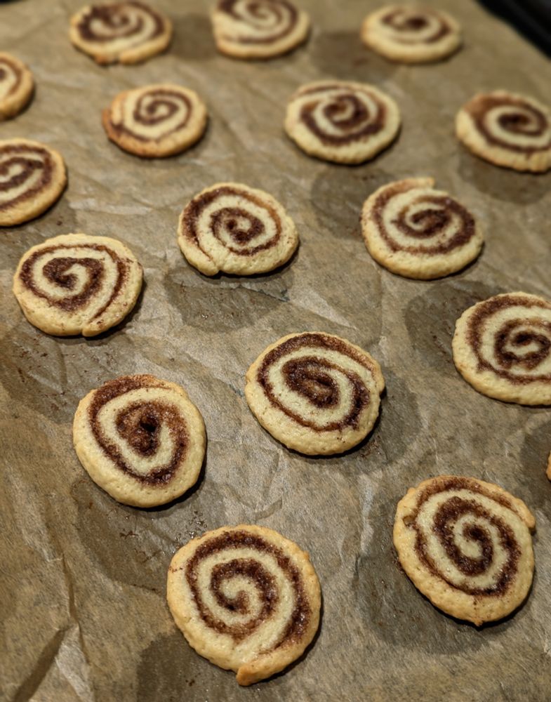 Weihnachtsplätzchen, die Zimtschnecken nachempfunden sind, auf einem Blech mit Backpapier 