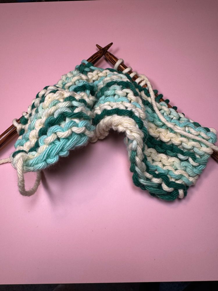 A piece of chunky garter stitch in shades of green on straight wooden knitting needles