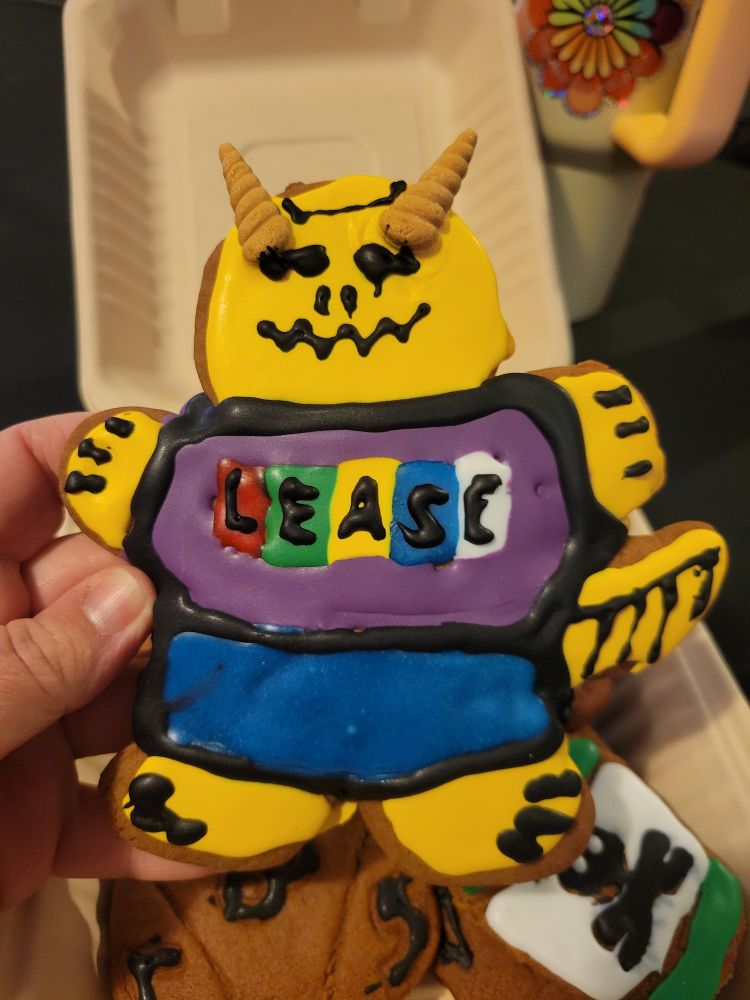 A gingerbread cookie decorated to look like a gold dragonborn with a T-shirt that says "LEASE".